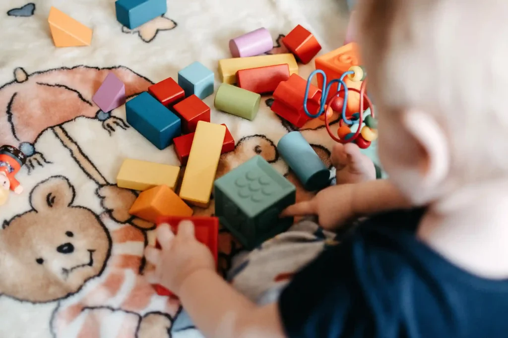 One year old baby reaching for a colorful wooden shape sorter on the floor