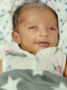 Newborn baby Eeshaan smiling while lying on a soft surface during diaper time