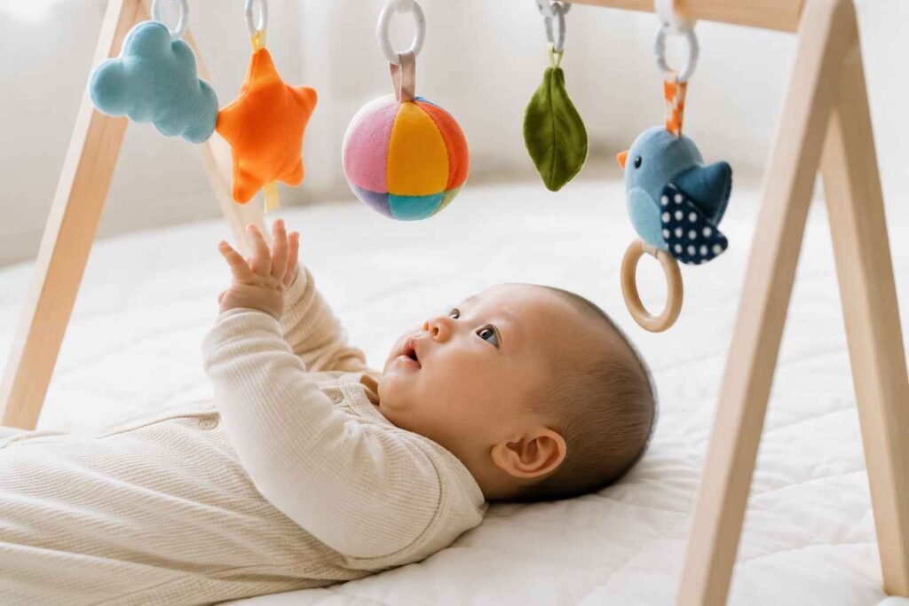 Baby 2 to 3 months old lying on white play mat reaching up toward hanging toys on activity gym during floor play