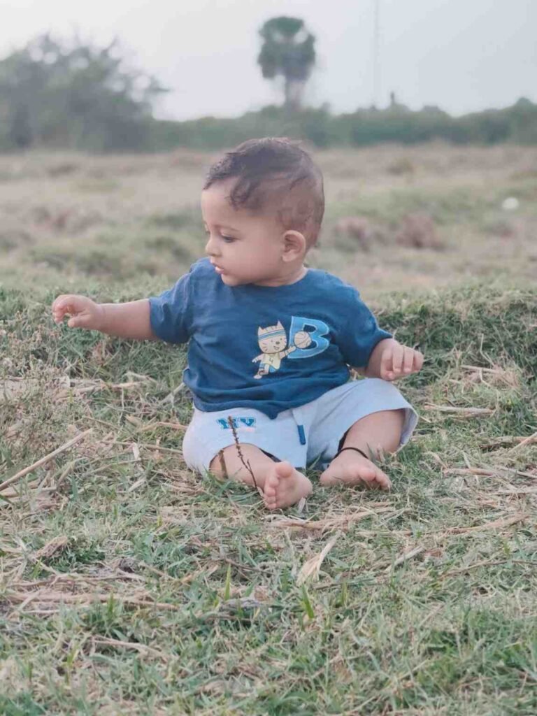 Baby Eeshaan sitting on grass and exploring it with his hands