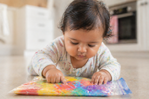 newborn pressing fingers into a sealed Ziploc bag filled with colorful yogurt paint during tummy time 