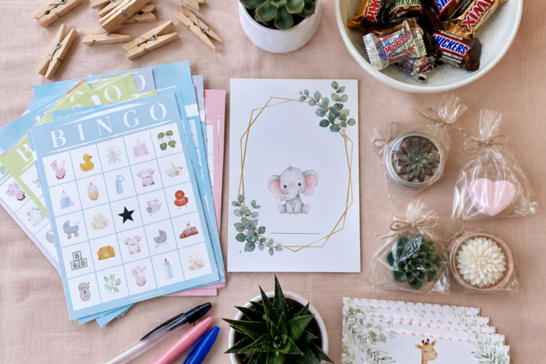Flat lay of baby shower game supplies including bingo cards, clothespins, pens, and small prizes on a pastel table