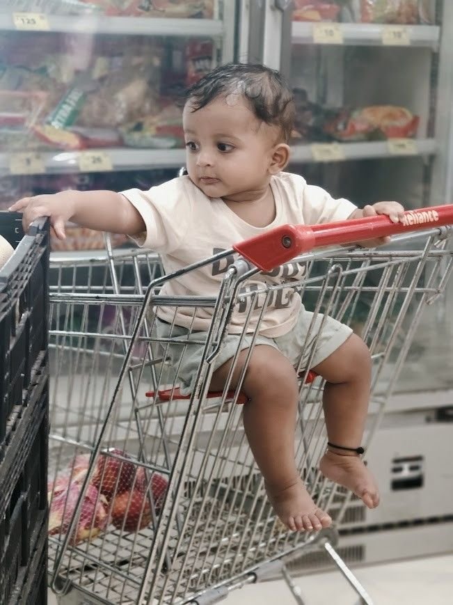 Toddler Eeshaan sitting in a supermarket basket, observing his surroundings as part of everyday learning through play and real-life experiences.