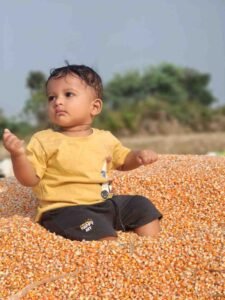 Baby Eeshaan sitting in a field and gently playing with corn seeds in his hands