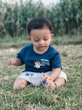 Toddler Eeshaan sitting outdoors and gently playing with grass, exploring nature through touch and curiosity as part of everyday learning.