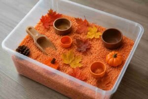 A colourful fall sensory bin with orange rice, mini pumpkins, and autumn leaves