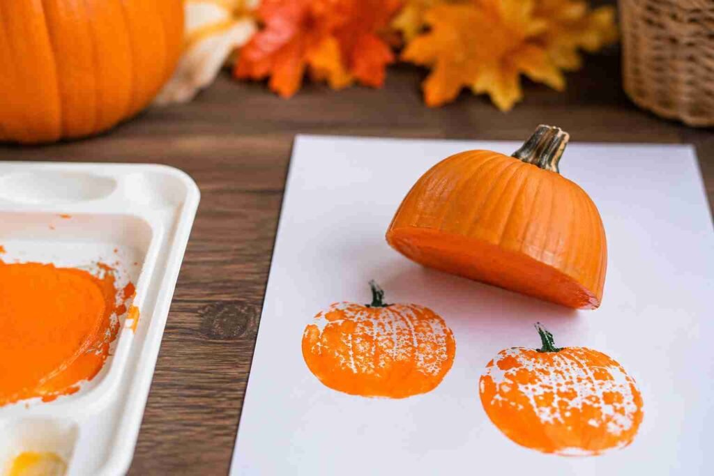 Real pumpkin half dipped in orange paint creating pumpkin stamp prints on white paper for an easy Halloween craft activity.
