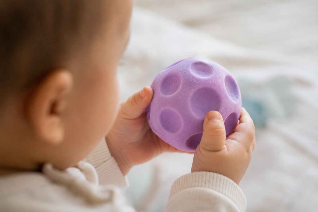 Infant hand gripping a textured auditory rattle toy