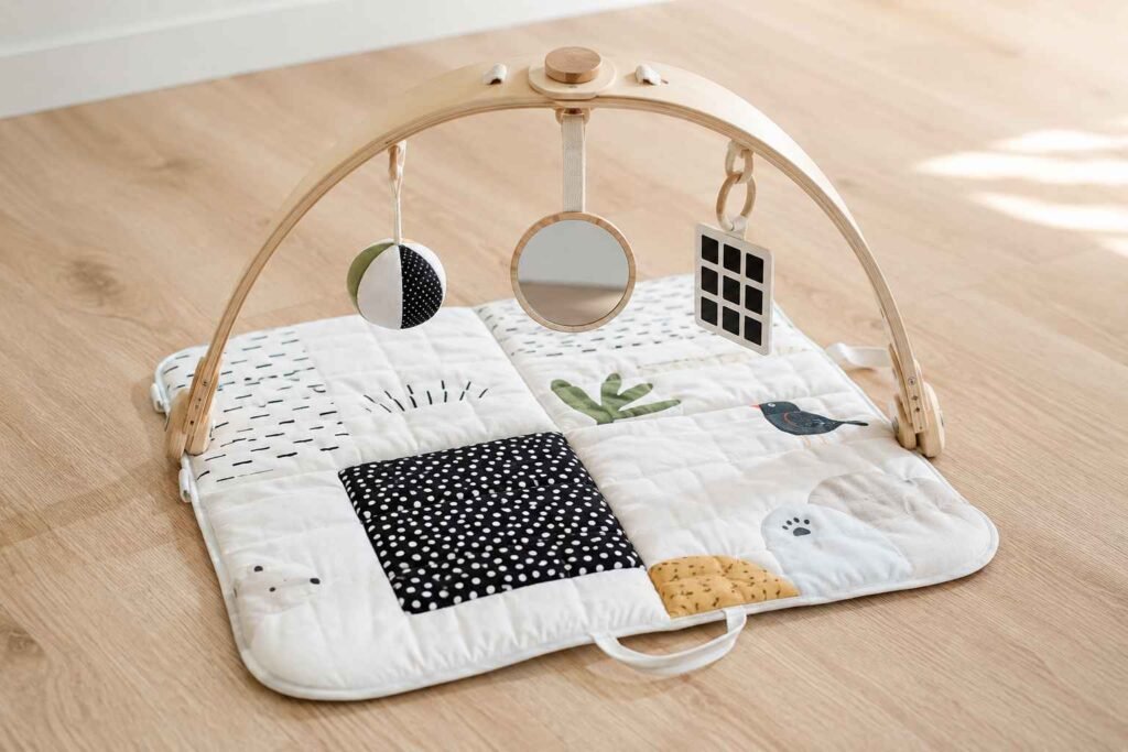 Lovevery Play Gym with wooden arch hanging toys black and white cards and baby safe mirror on patterned play mat for newborn and 3 month old development