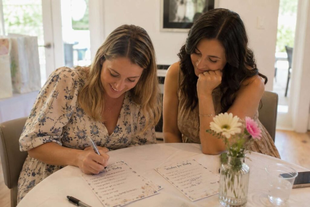 Woman writing on a Wishes for Baby card at a baby shower table with flowers and pens nearby